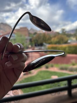 Two metal spoons bent by hand, held up against a blurred outdoor backdrop in Sedona, Arizona, representing the power of mindset and intention.