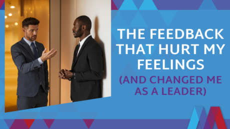 Feature Image For The Blog 'The Feedback That Hurt My Feelings (And Changed Me As A Leader)' Showing Two Male Colleagues In An Office Hallway, One Giving Feedback With An Open Hand Gesture.