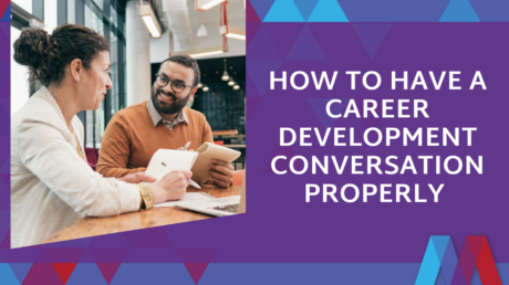 A Manager Takes Notes While Talking With A Smiling Team Member Across A Table In A Bright Office, Next To The Blog Title "How To Have A Career Development Conversation Properly" On A Purple Mosaic PD Background.