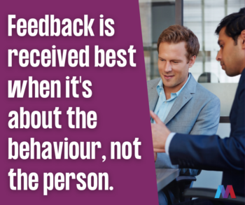 A man in a grey blazer listens to a colleague across a desk, next to the quote “Feedback is received best when it’s about the behaviour, not the person,” with the Mosaic People Development logo.
